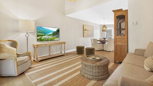 A modern living room with a flat-screen TV, a sofa, a chair, a coffee table, and a dining area with a table and chairs.