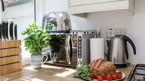 Una cocina con tostadora, hervidor y un plato de pan y tomates.