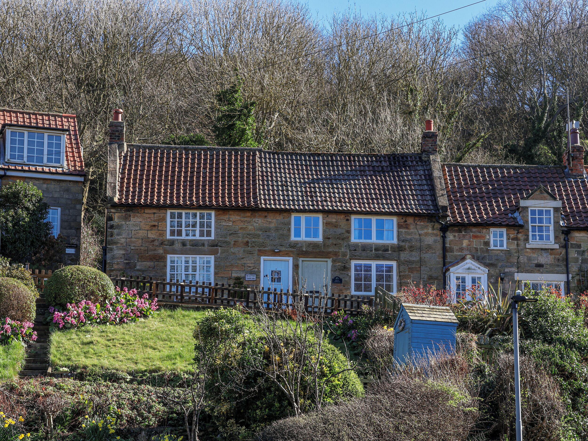 A stone house with a tiled roof, a wooden fence, and a garden with flowers.