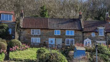 A stone house with a tiled roof, a wooden fence, and a garden with flowers.