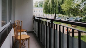 A balcony with two wooden chairs and a table, overlooking a street with parked cars and trees. - Apartamenty Sun & Snow Kopernika 16 (Ustka)