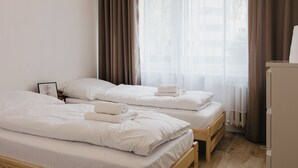 A hotel room with two single beds, a wooden nightstand, a framed picture, and a view of the outside through sheer curtains. - Apartamenty Sun & Snow Kopernika 16 (Ustka)