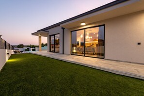 Une maison moderne avec une pelouse bien entretenue, de grandes portes-fenêtres coulissantes donnant sur un coin repas et une cuisine ouverte.