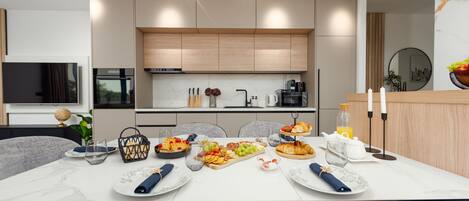 A modern kitchen with built-in appliances, a dining area with a marble table, and a breakfast spread.