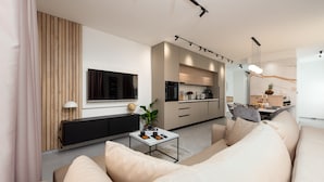 Una sala de estar moderna con un sofá, una mesa de centro y un televisor. Hay una cocina con armarios y una mesa de comedor.