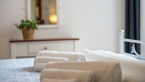 Ein ordentlich bezogenes Bett mit weißen Handtüchern, einem kleinen Topfpflänzchen und einem Spiegel auf einer weißen Kommode.