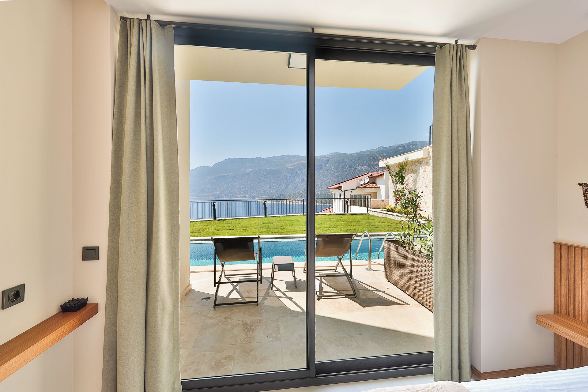 A balcony with a pool, a table, and chairs, overlooking a mountainous landscape.