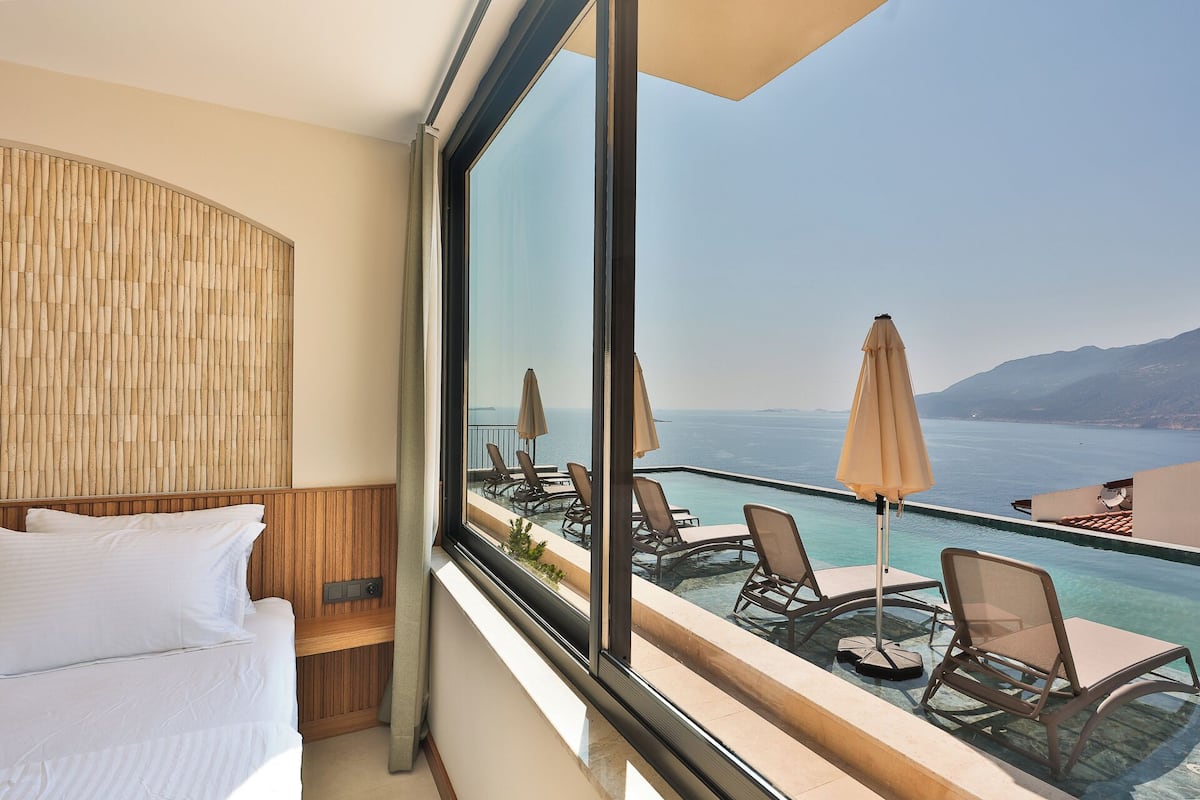 A balcony with a view of the sea, a bed, and a wooden wall.
