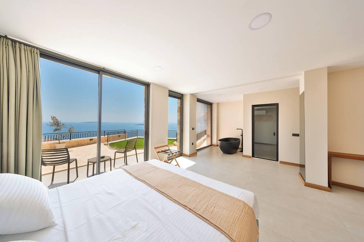 A hotel room with a large bed, a small balcony with a table and chairs, and a view of the sea.