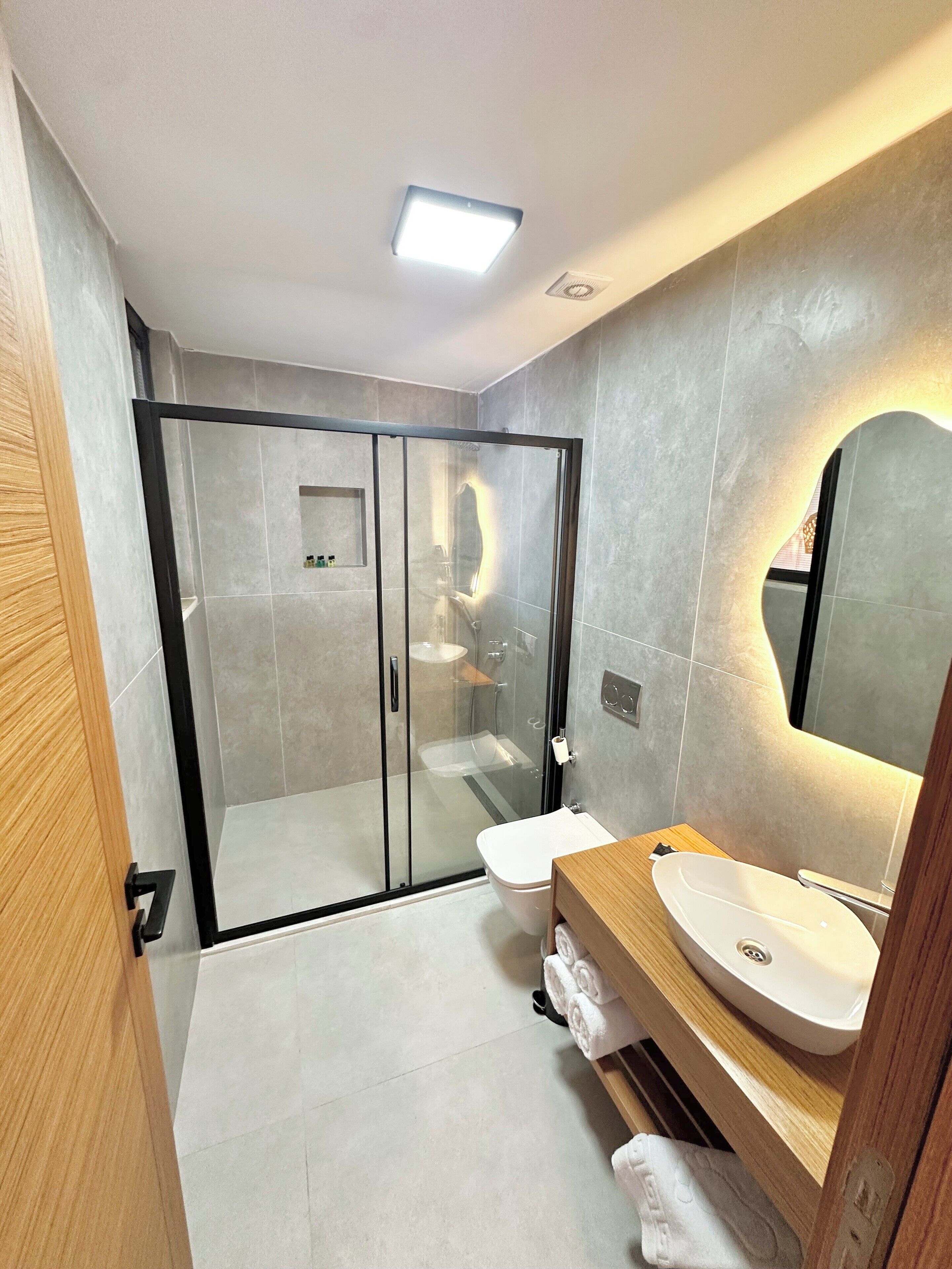 A modern bathroom with a glass-enclosed shower, a wooden vanity with a sink, and a large mirror.