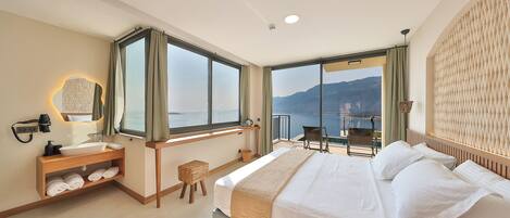 A hotel room with a bed, a desk, a mirror, a window with a view of the sea, and a balcony with a chair.