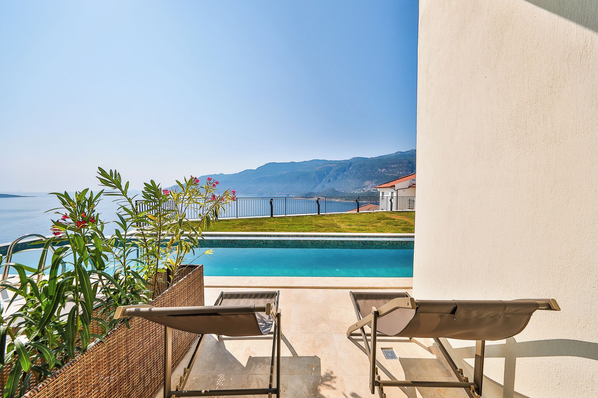 A poolside view with two lounge chairs, a clear view of the sea, and a mountain in the background.