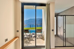 Habitación de hotel moderna con puerta de vidrio corrediza que da a un balcón con piscina y vistas al mar y a las montañas.