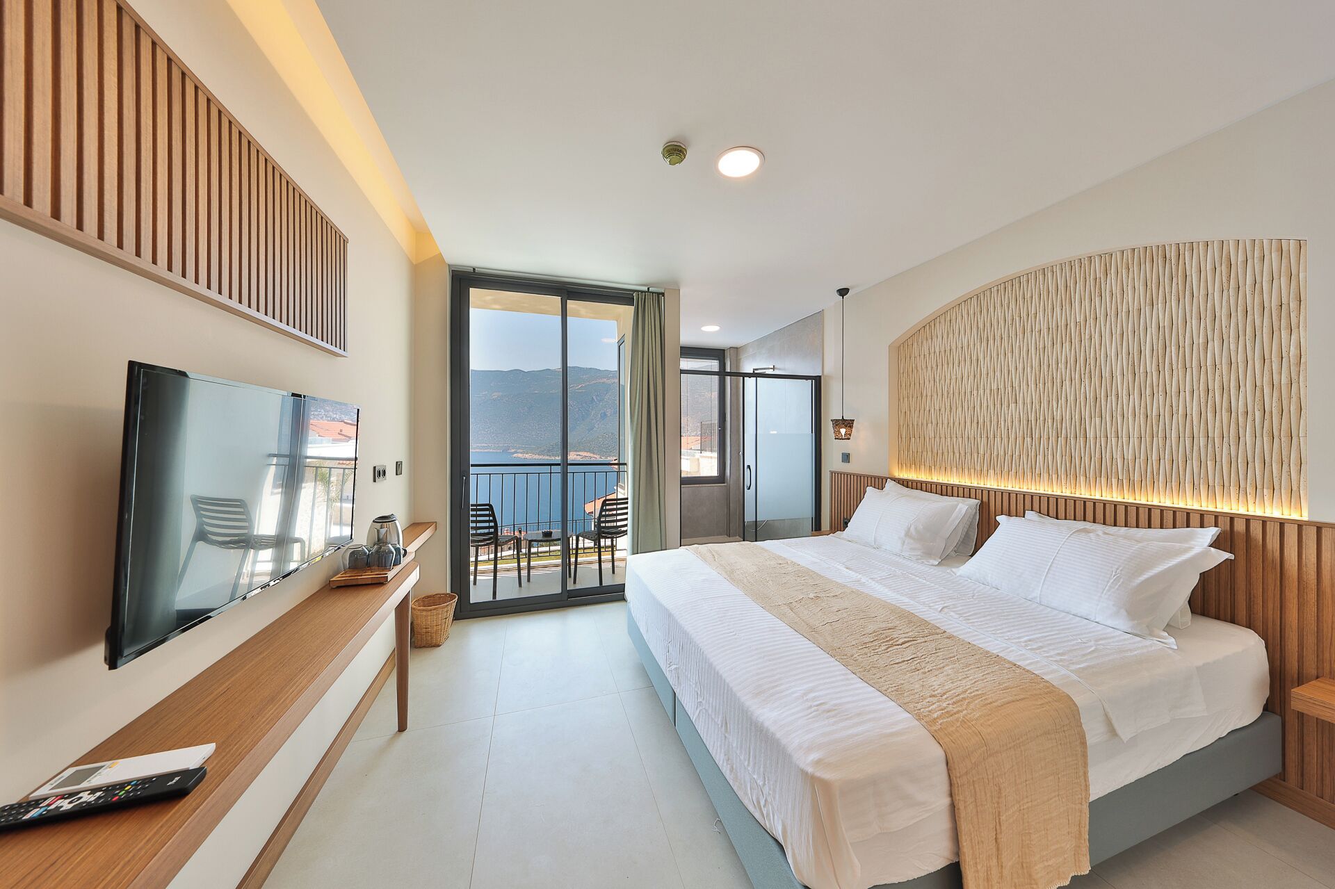 A modern hotel room with a large bed, a TV, and a balcony with a view.