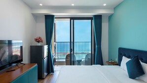 A hotel room with a bed, a TV, a refrigerator, a small table with chairs, and a balcony with a view of the sea. - Phu Quoc Sea View Apartment (Phu Quoc)