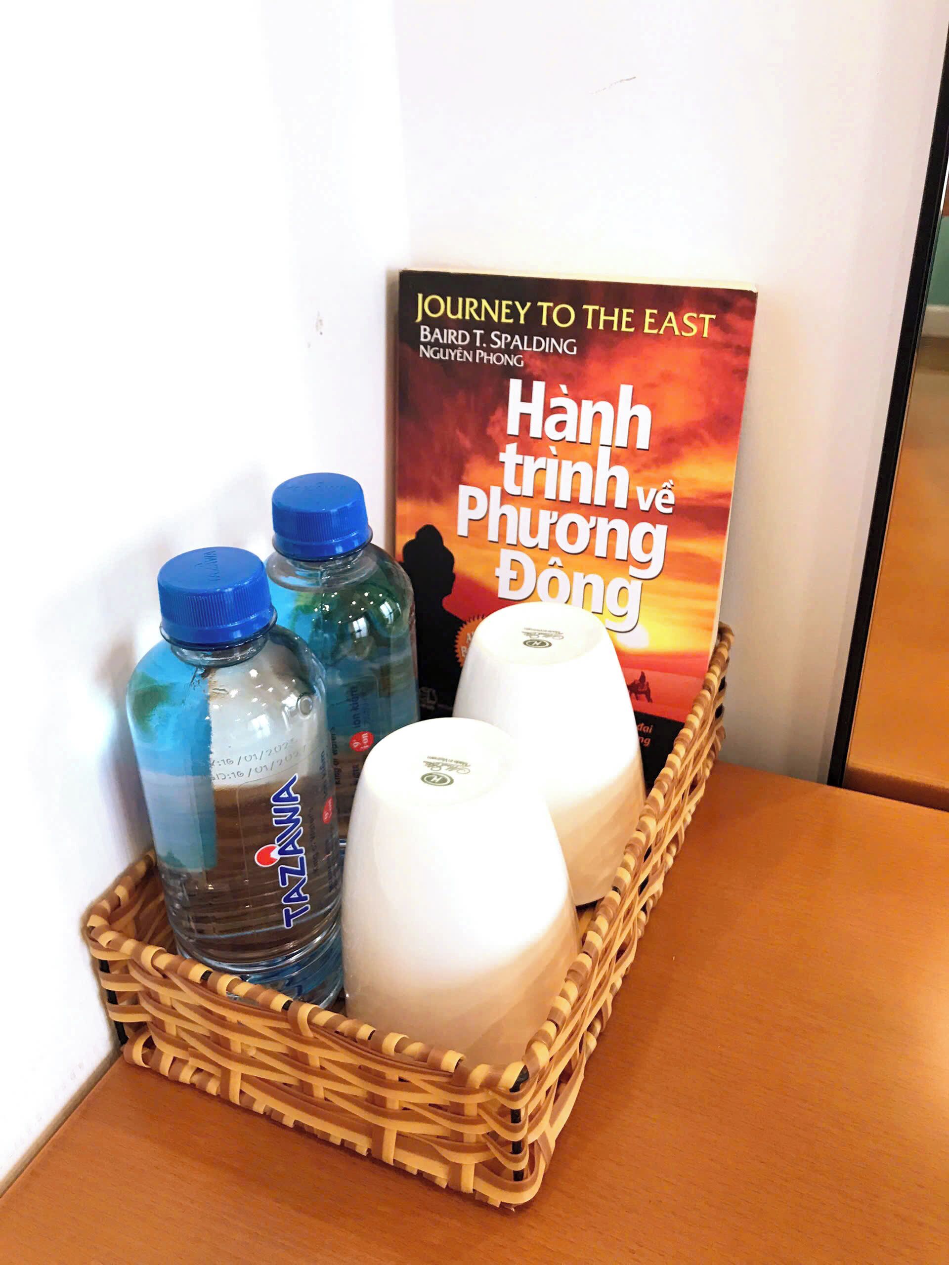 A wicker basket containing bottled water and a book titled 'Journey to the East' by Baird T. Spalding.