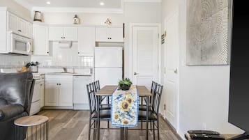 Una cocina moderna con armarios blancos, una mesa de comedor con camino de mesa de girasol y un sofá de cuero negro.