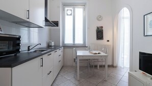 Cocina moderna con microondas, lavamanos y ventana. Hay una mesa de comedor con sillas y un reloj en la pared.