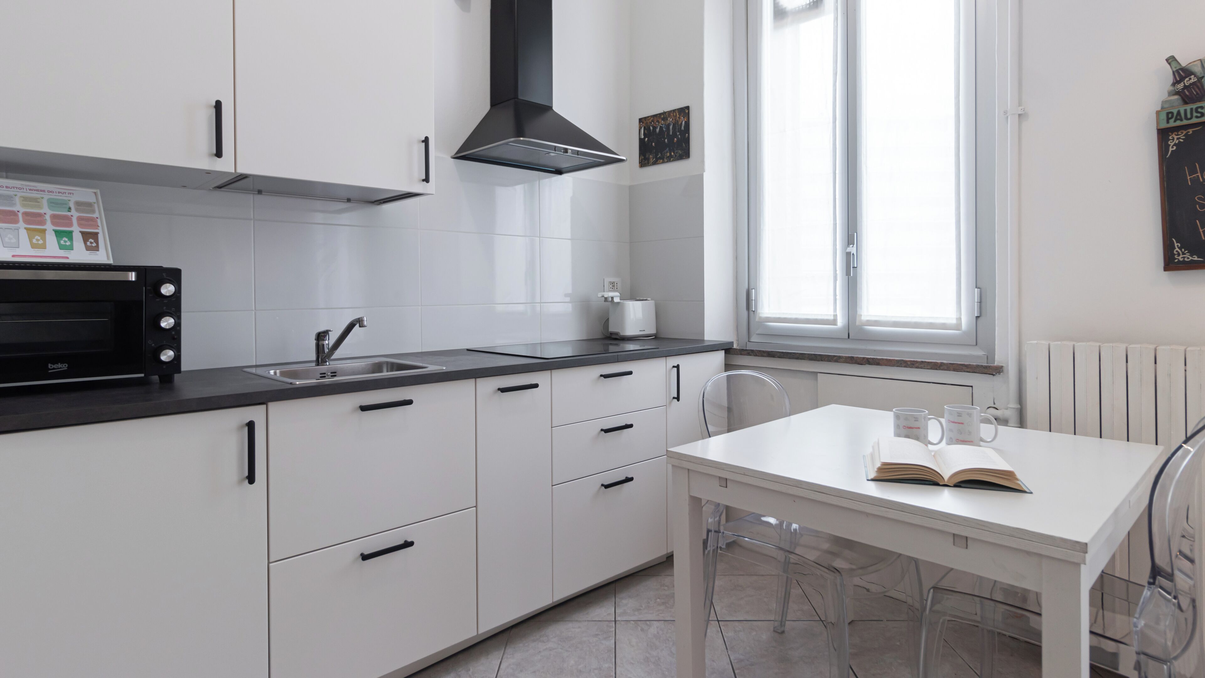 Une cuisine moderne avec des meubles blancs, un micro-ondes noir et une fenêtre qui laisse entrer la lumière naturelle.