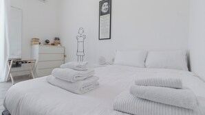 Una cama bien hecha con toallas dobladas, un aparador blanco y un retrato enmarcado en la pared.