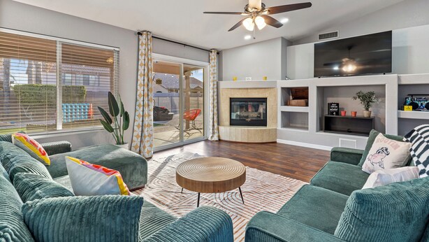 A modern living room with a green sofa set, a fireplace, a flat-screen TV, and a ceiling fan. - Vibrant Home – Heated Pool, Arcade, & Fire pit (Phoenix)