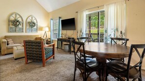 A dining area with a round table, chairs, a television, and a window with curtains. - Warm Welcome Getaway Resort Stay for 6 With Amenities Near Downtown (Branson)