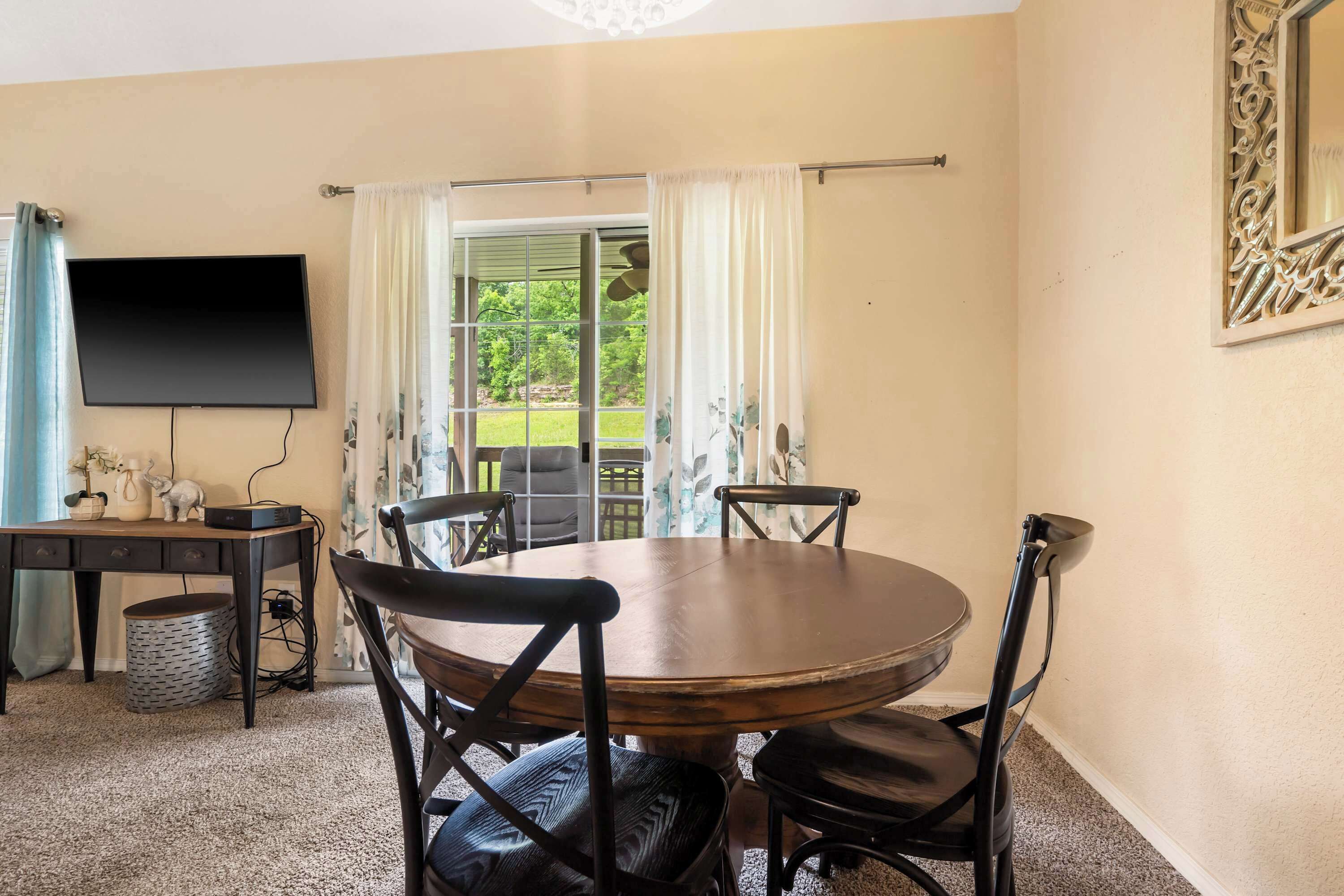 Un comedor con una mesa redonda y cuatro sillas, un televisor montado en la pared, y una ventana con cortinas.