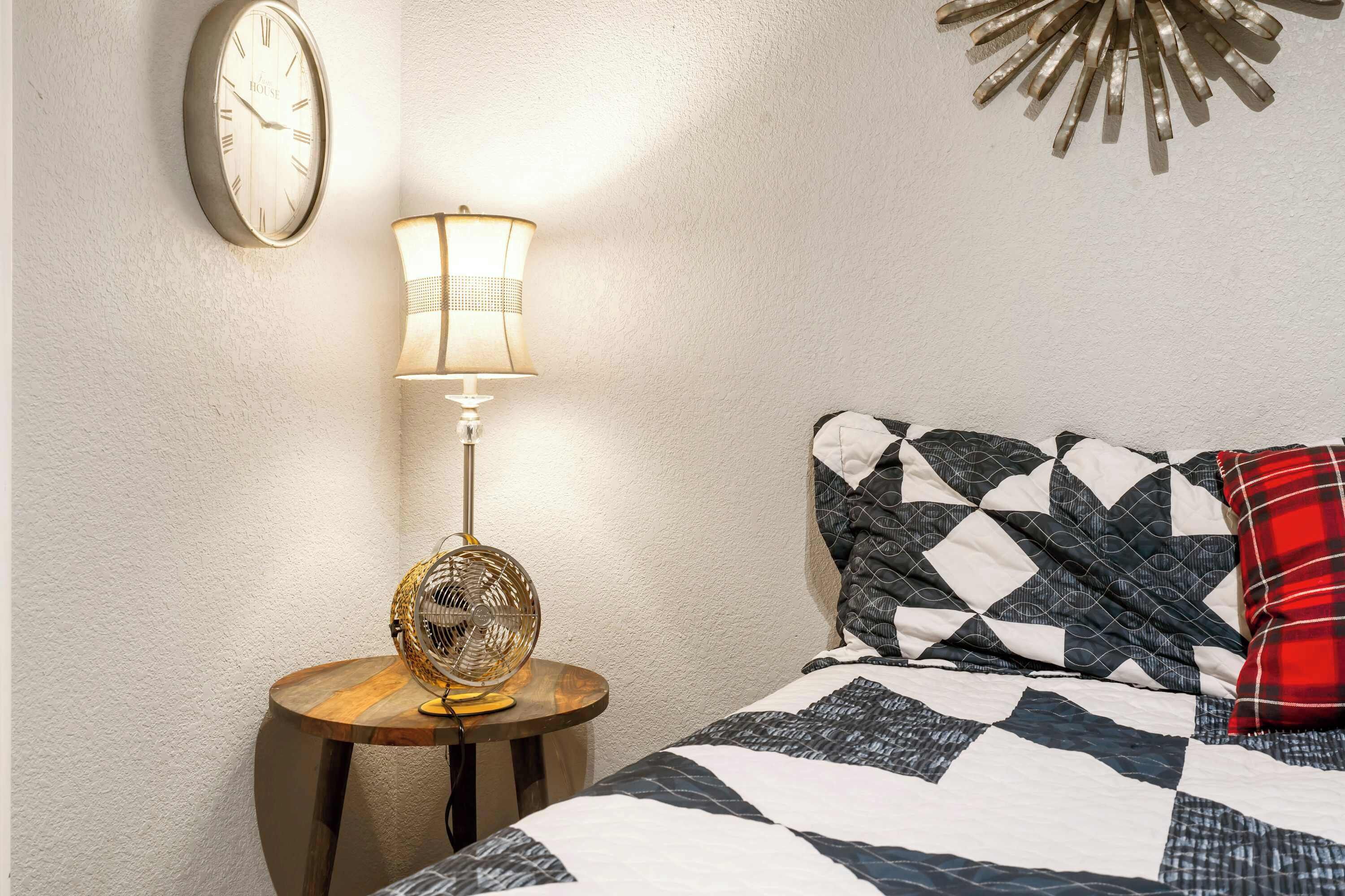 A bedroom with a bed, a wall clock, a lamp, and a decorative wall piece.