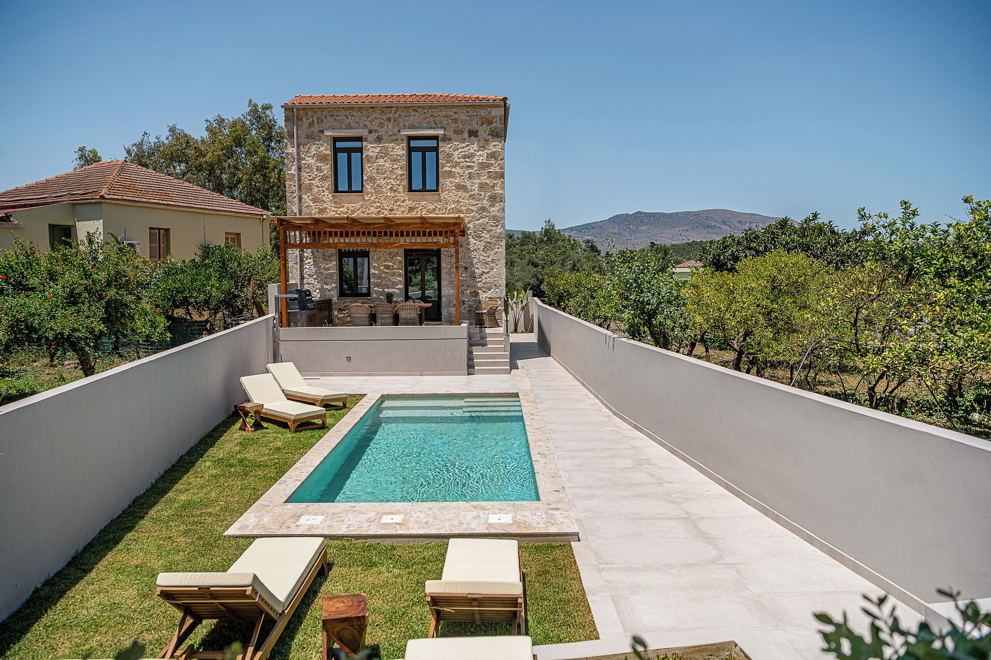 A modern villa with a swimming pool, outdoor seating, and a view of the surrounding landscape.