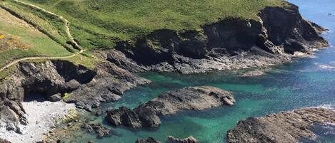 A coastal landscape with a winding path, rocky cliffs, and clear blue waters.