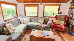 A cozy living room with a grey sectional sofa, a red armchair, a wooden coffee table, and a bookshelf filled with books. - The Tree House (Haverfordwest)