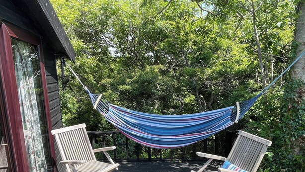 A wooden deck with a hammock and two wooden chairs. - The Tree House (Haverfordwest)