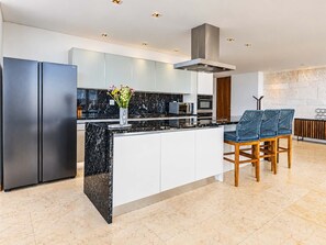 Een moderne keuken met een marmeren eiland, roestvrijstalen apparatuur en een zithoek met blauwe stoelen.