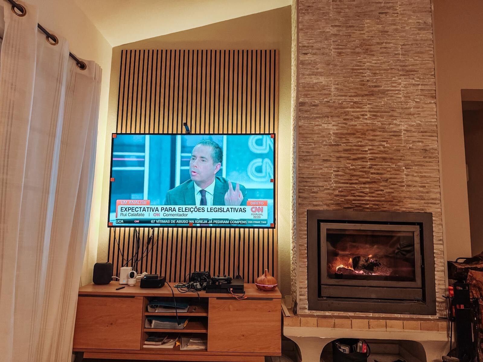 Un saló amb televisió penjada a una paret de fusta, una llar de foc i un moble d'entreteniment de fusta amb aparells electrònics.