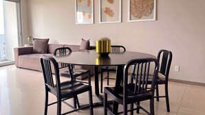 Ein stilvolles Wohnzimmer mit einem runden Esstisch, schwarzen Stühlen, einer Couch und drei gerahmten Blätterbildern an der Wand.