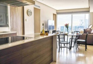 A modern kitchen with a central island, dining area with chairs, a large window with a city view, and a built-in oven. - 2BR retreat close to Colomos w/ gym (Guadalajara)
