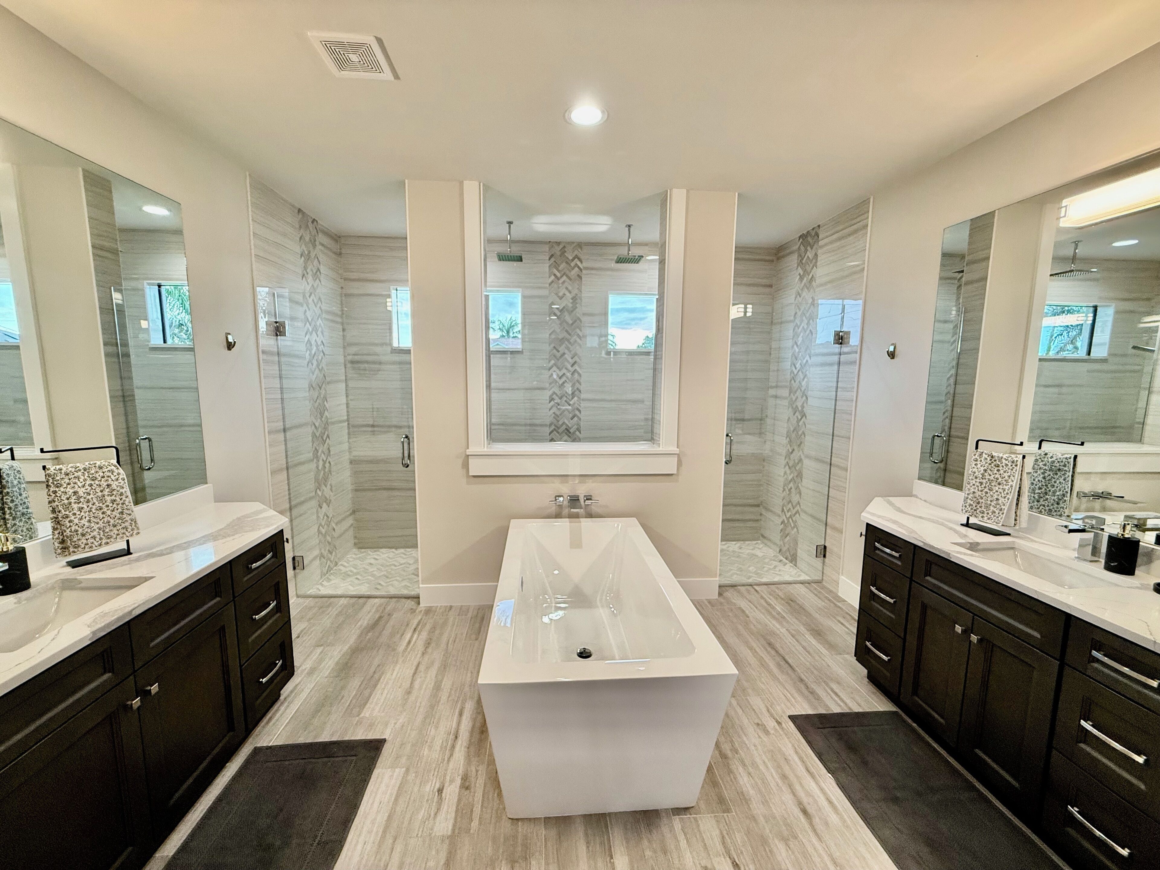A modern bathroom with a central rectangular sink, two vanity mirrors, and a shower with a glass door.