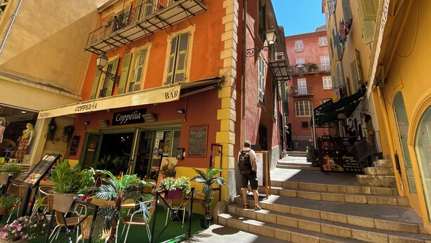 A narrow street with buildings on either side, featuring outdoor seating areas with tables and chairs, and a staircase leading to an upper floor. - Superb studio with sleeping area! Old Nice! (Nice)