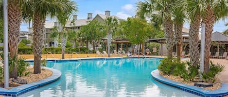 A swimming pool with palm trees and lounge chairs, surrounded by buildings.