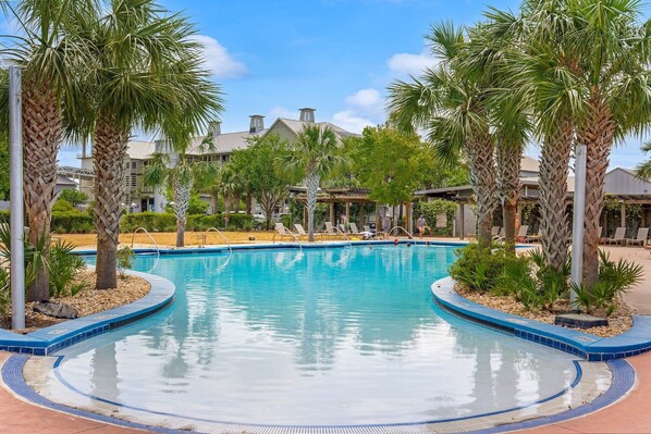 A swimming pool with palm trees and lounge chairs, surrounded by buildings.