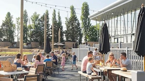 Un espace de restauration en plein air avec des tables et des bancs en bois, entouré d’une terrasse en bois et illuminé de guirlandes lumineuses.