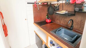 Et lille køkken med vask, en rød elkedel, en mikrobølgeovn og diverse køkkenredskaber.
