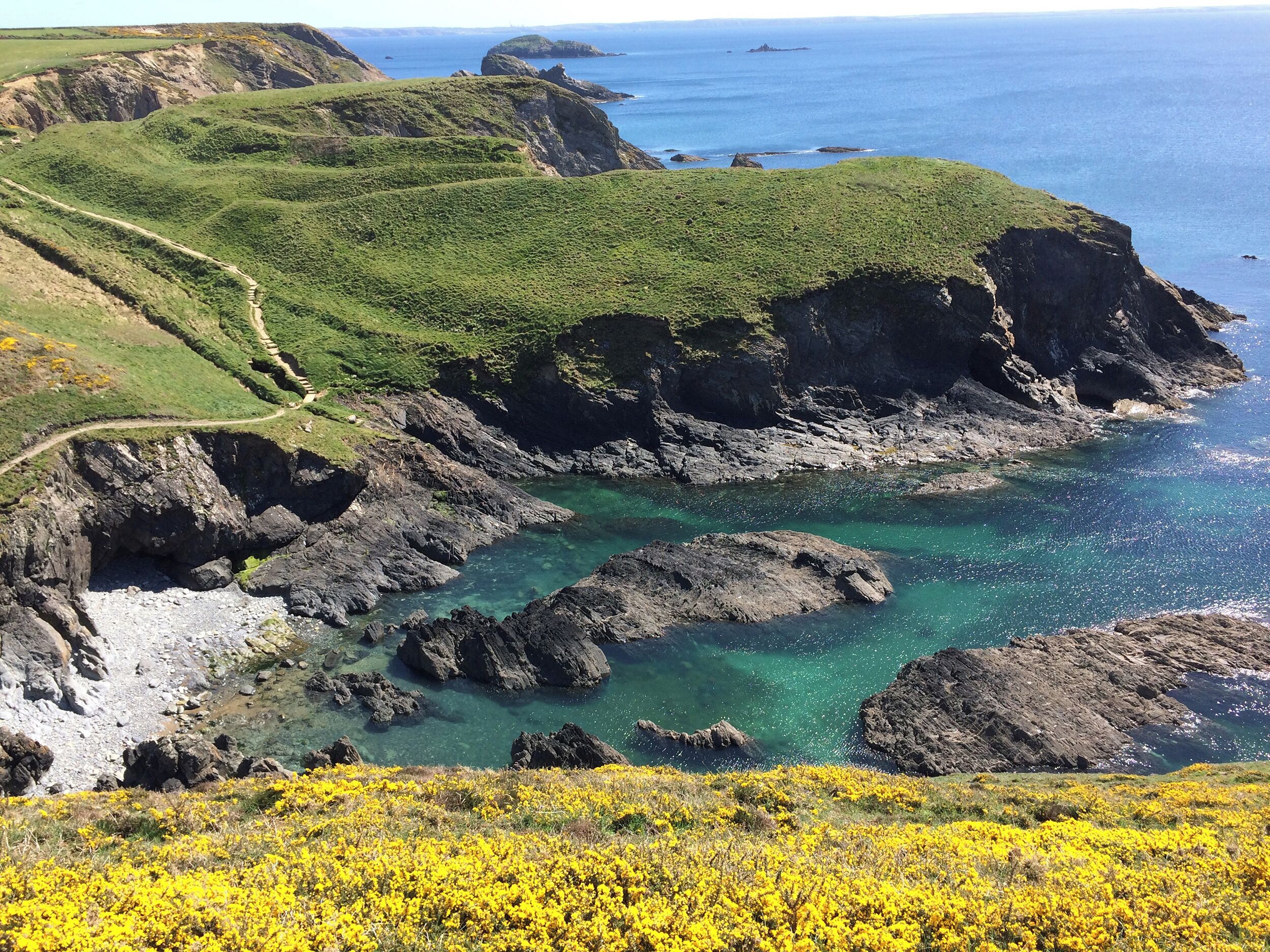 A coastal landscape with rocky cliffs, clear blue waters, and a winding path.