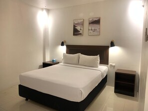 A neatly made bed with white linens, two bedside tables with lamps, and two framed pictures on the wall. - Hotel Harmony (Batulicin)