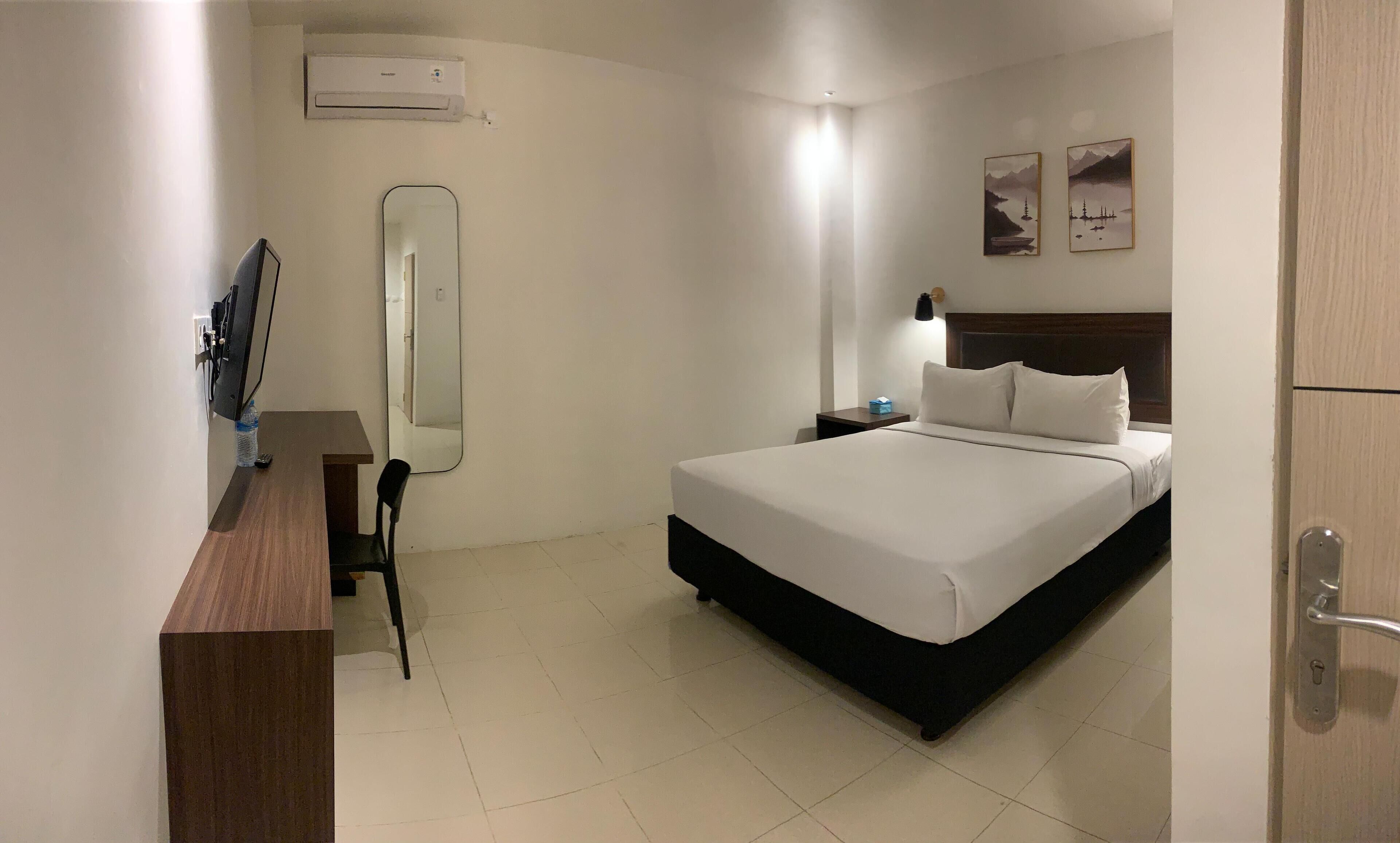 A hotel room with a bed, a desk, a chair, a mirror, a nightstand, and wall-mounted artwork.
