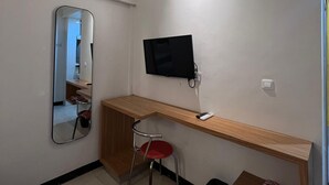 A small room with a wooden desk, a red chair, a TV mounted on the wall, and a mirror on the wall. - Hotel Harmony (Batulicin)