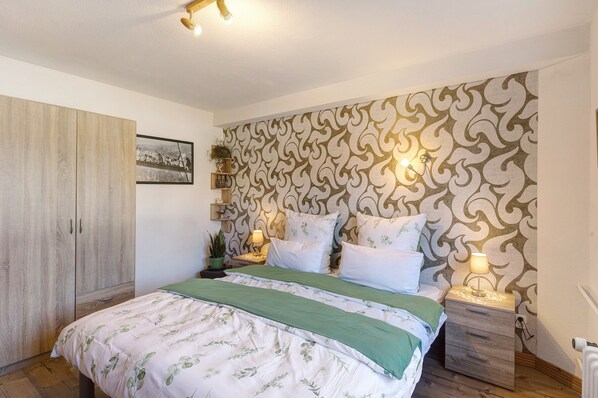 Un dormitorio con cama, mesitas de noche, armario y papel tapiz estampado.