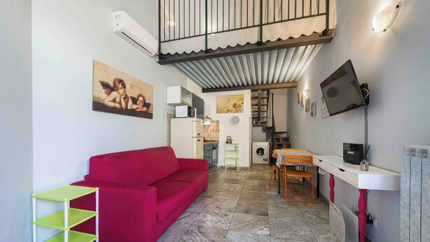 A compact living space with a red sofa, a small kitchen area, a dining table, and a TV mounted on the wall. - Romito Loft by MMega (Florence)