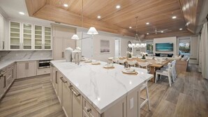 A spacious kitchen with a large island, wooden ceiling, and modern lighting.