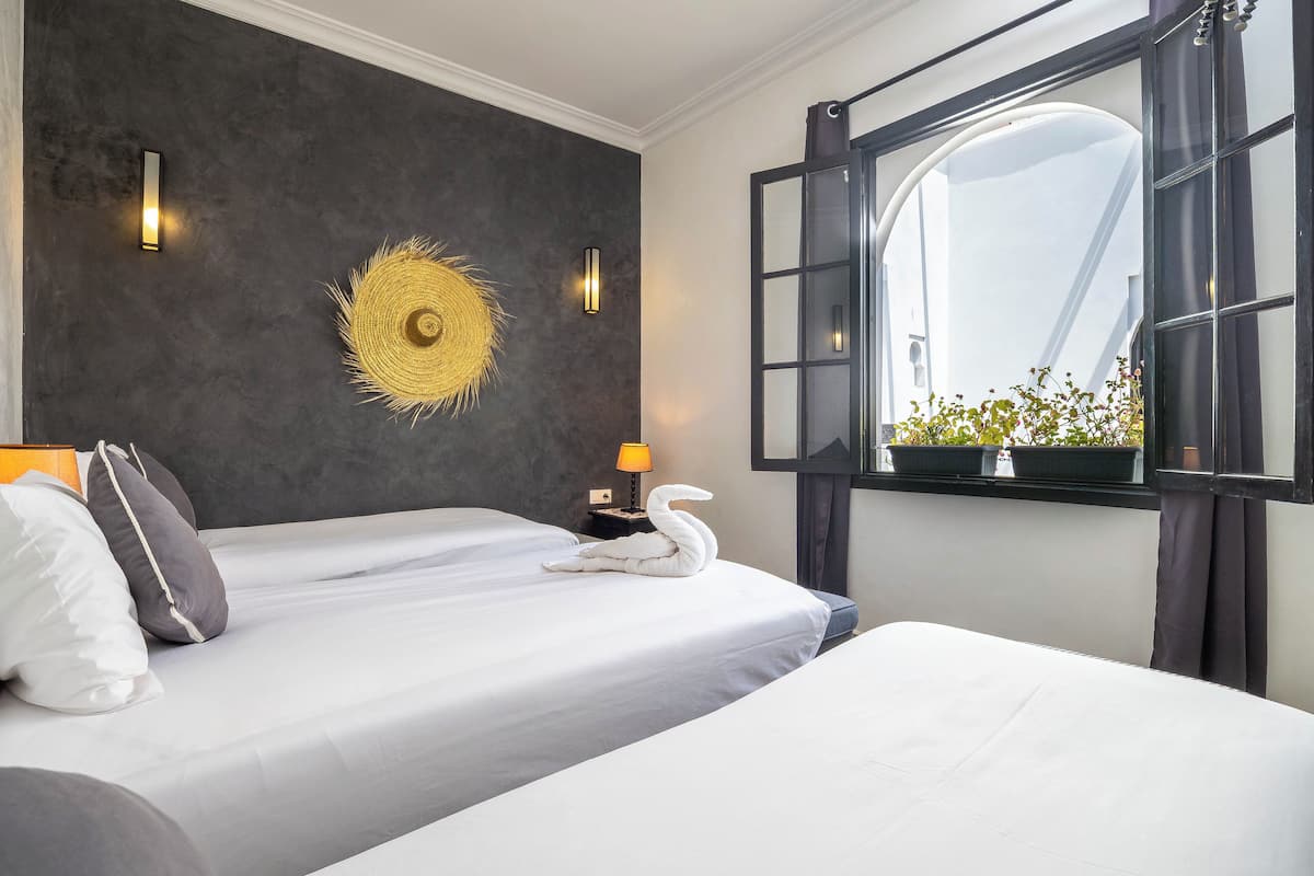 Ein Hotelzimmer mit einem Bett, einer Wandlampe, einem Wandbild und einem Fenster mit Blick auf Pflanzen.